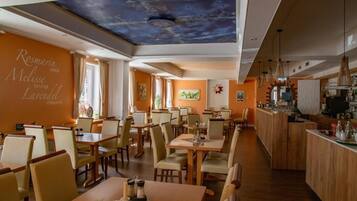 Um restaurante com um balcão comprido, várias mesas e cadeiras.