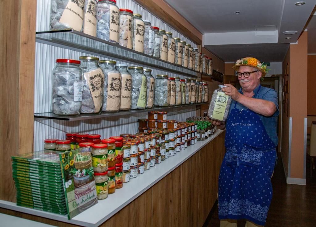 A person in an apron standing in front of shelves stocked with jars of preserved food.