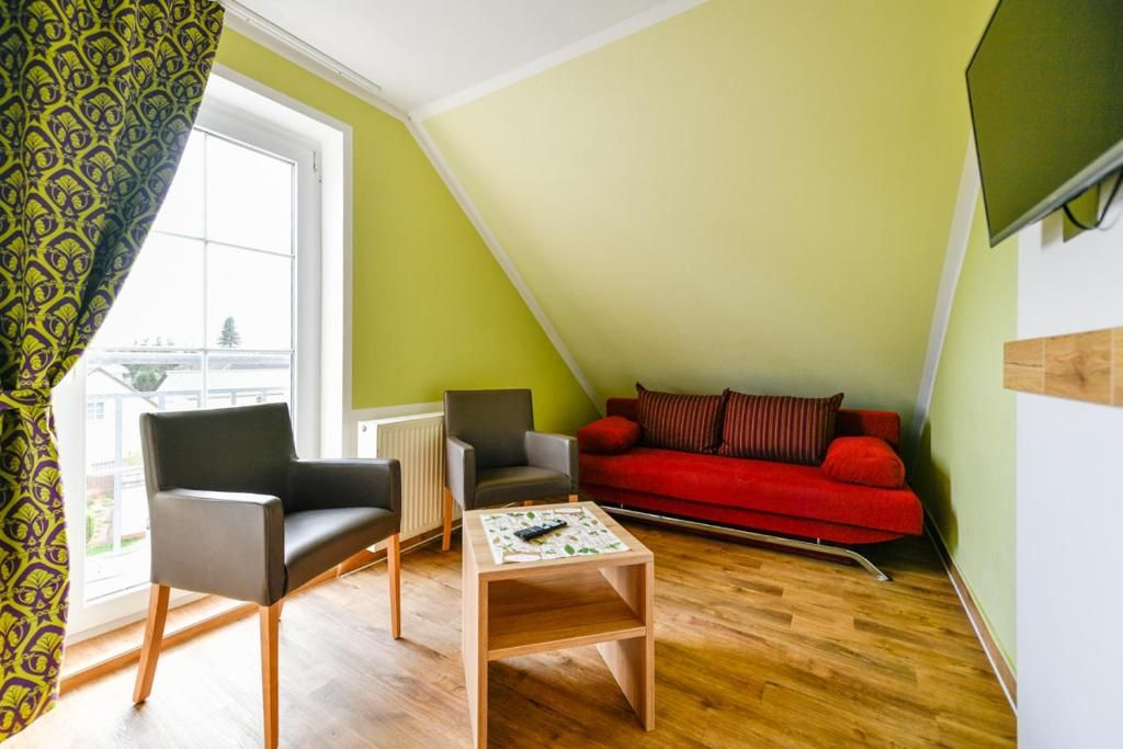 A room with a red sofa, two chairs, a small wooden table, and a window with a view.