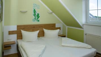 A bedroom with a sloped ceiling, a bed with white bedding, a wooden headboard, bedside tables, and a window with a view.