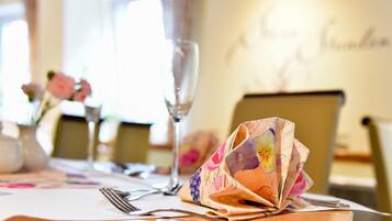 A dining table with a floral tablecloth, a folded menu, and a glass of water.