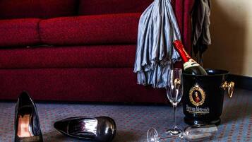 Una habitación con un sofá rojo, un cubo negro con un emblema dorado, una botella de champán, una copa de vino y un par de zapatos de tacón negros sobre una alfombra estampada.