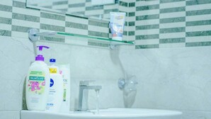Un baño con un lavabo blanco, un estante de vidrio encima y artículos de aseo en el estante.