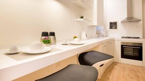 A modern kitchen with a white countertop, two black bar stools, a built-in oven, and a stainless steel kettle. - Dante 58 (Palermo)
