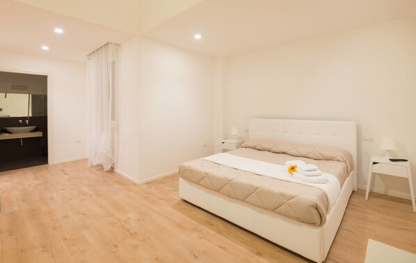 A modern bedroom with a large bed, a bedside table, a nightstand, and a bathroom visible through an open door.