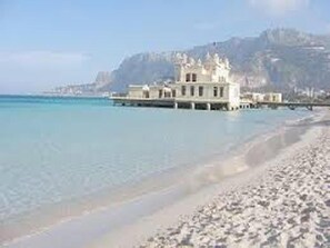 A beachfront property with a large building, clear blue waters, and a mountainous backdrop.