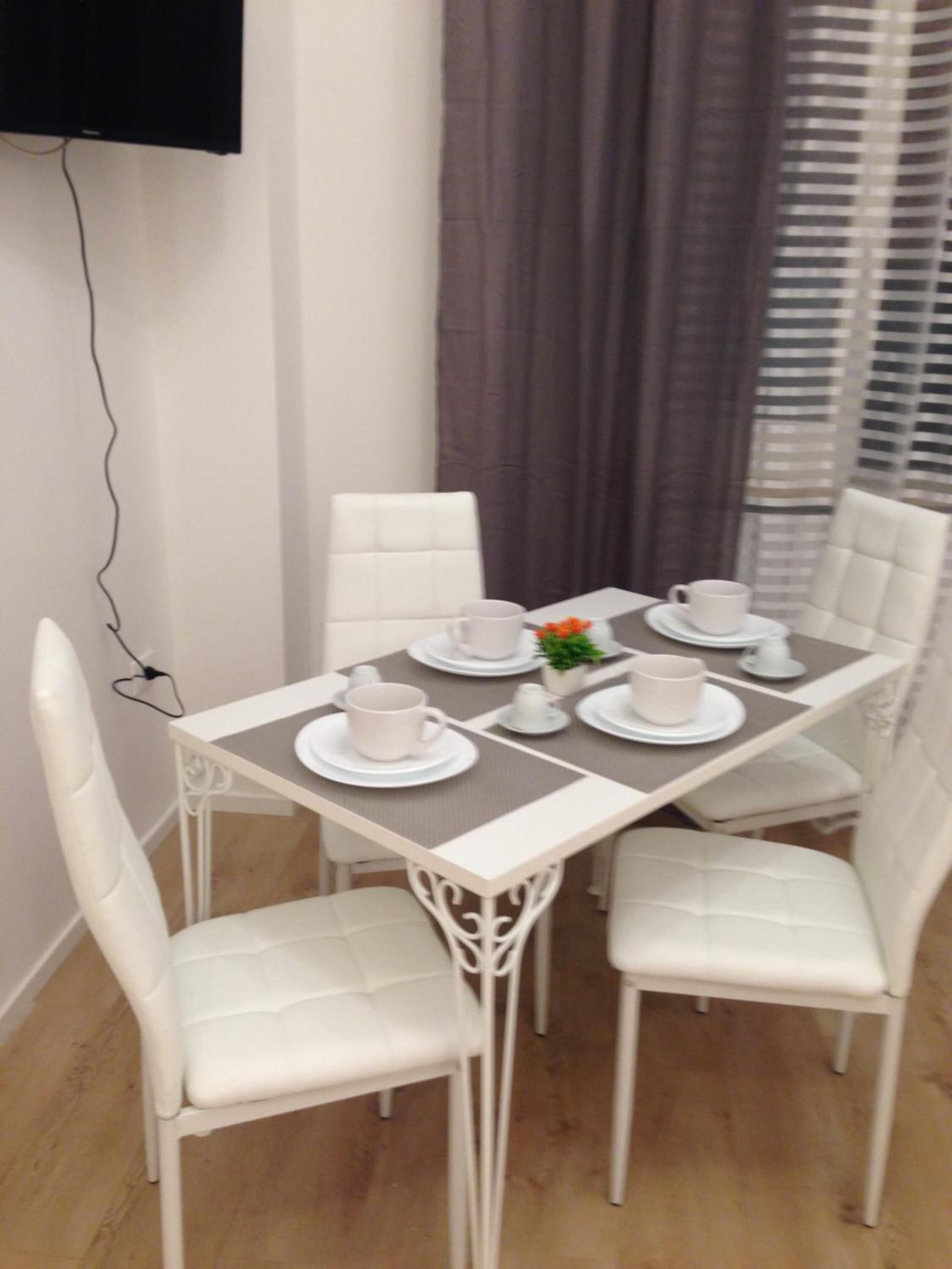 A dining area with a white table set for four, white chairs, and a small potted plant.
