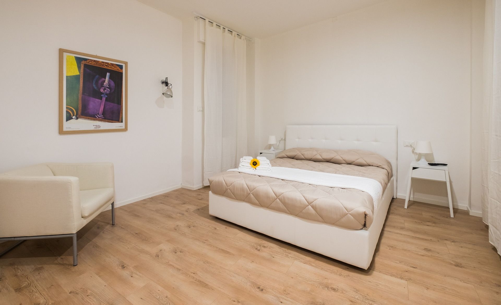 A bedroom with a bed, a chair, a nightstand, and a painting on the wall.