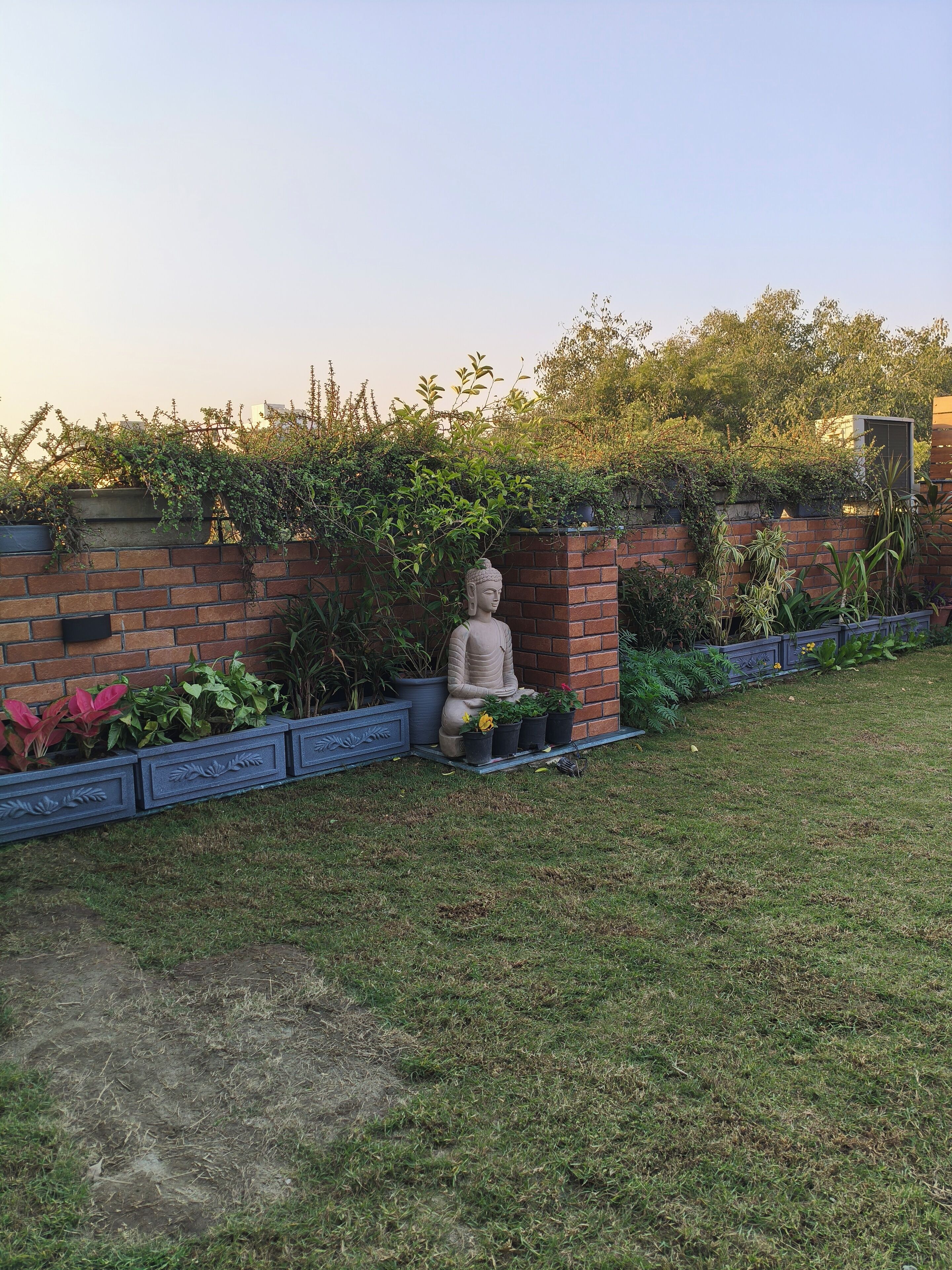 A garden with a Buddha statue, brick wall, and various plants.