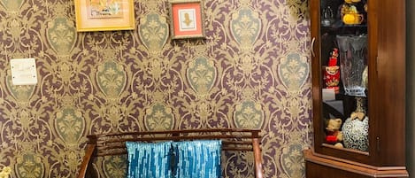 A traditional room with a wooden bed, patterned wallpaper, and a cabinet with decorative items.