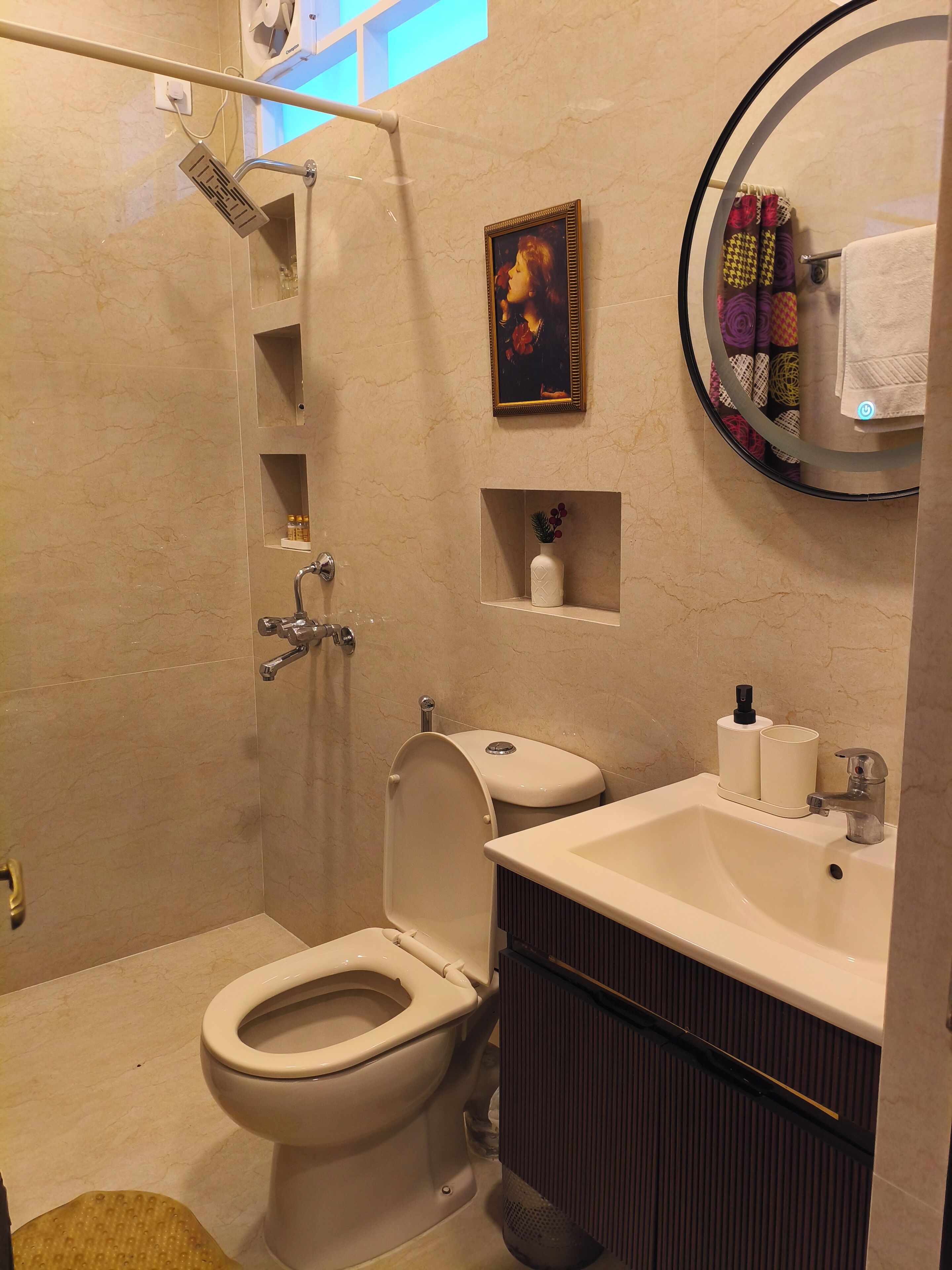A bathroom with a toilet, sink, shower, and a framed picture on the wall.