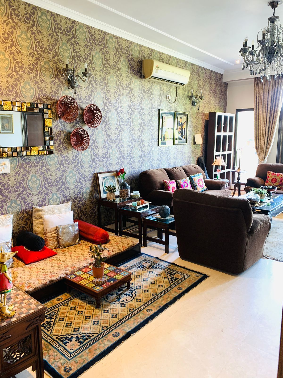 A living room with patterned wallpaper, a brown sofa, a coffee table, and a chandelier.