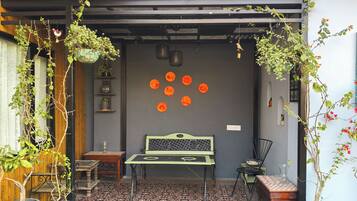 Uma área de estar externa aconchegante com uma mesa e cadeiras, rodeada por vasos de plantas e uma parede decorativa com padrões circulares laranja.