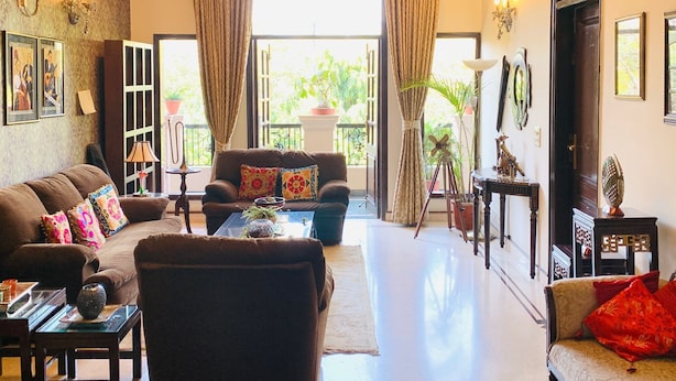 A spacious living room with a sofa set, a coffee table, and a chandelier. There are curtains, a fan, and a door leading to an outdoor area. - vandanas bed and breakfast (New Delhi)