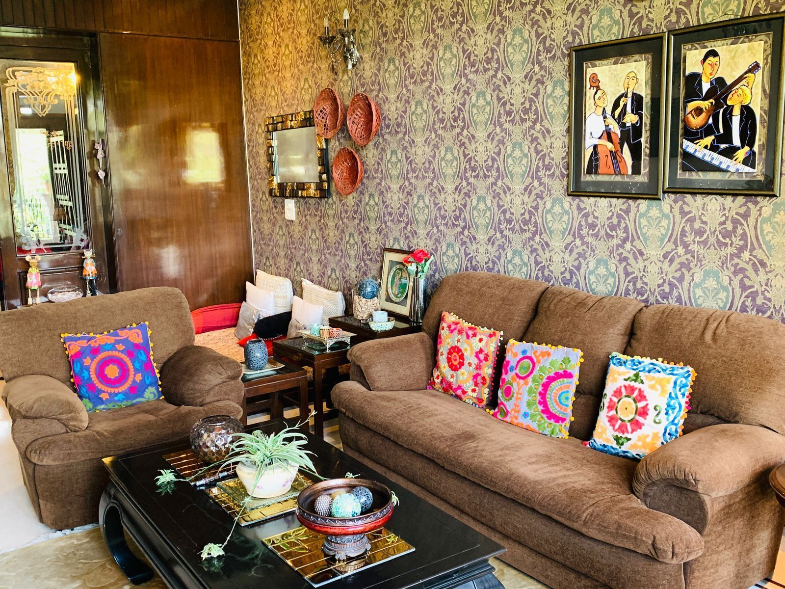 Un salon avec un ensemble de canapés marron, des coussins colorés, une table basse noire agrémentée d'objets décoratifs et un papier peint à motifs.