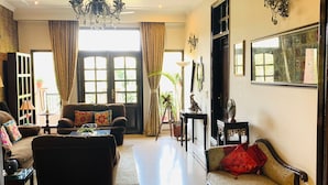 A spacious living room with a large window, a chandelier, and a sofa with a red cushion. - vandanas bed and breakfast (New Delhi)