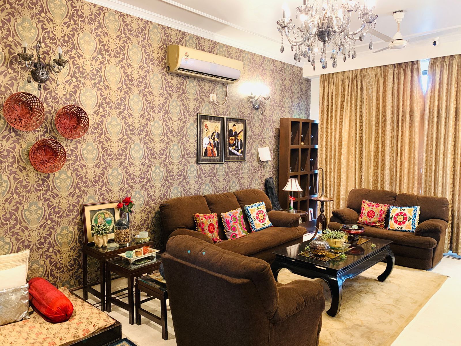 A living room with patterned wallpaper, a chandelier, a ceiling fan, and a brown sofa set.
