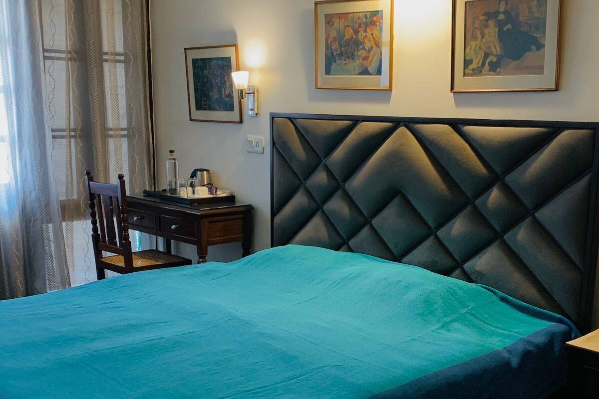 A bedroom with a bed, a nightstand, a chair, and a desk. There are three framed pictures on the wall.