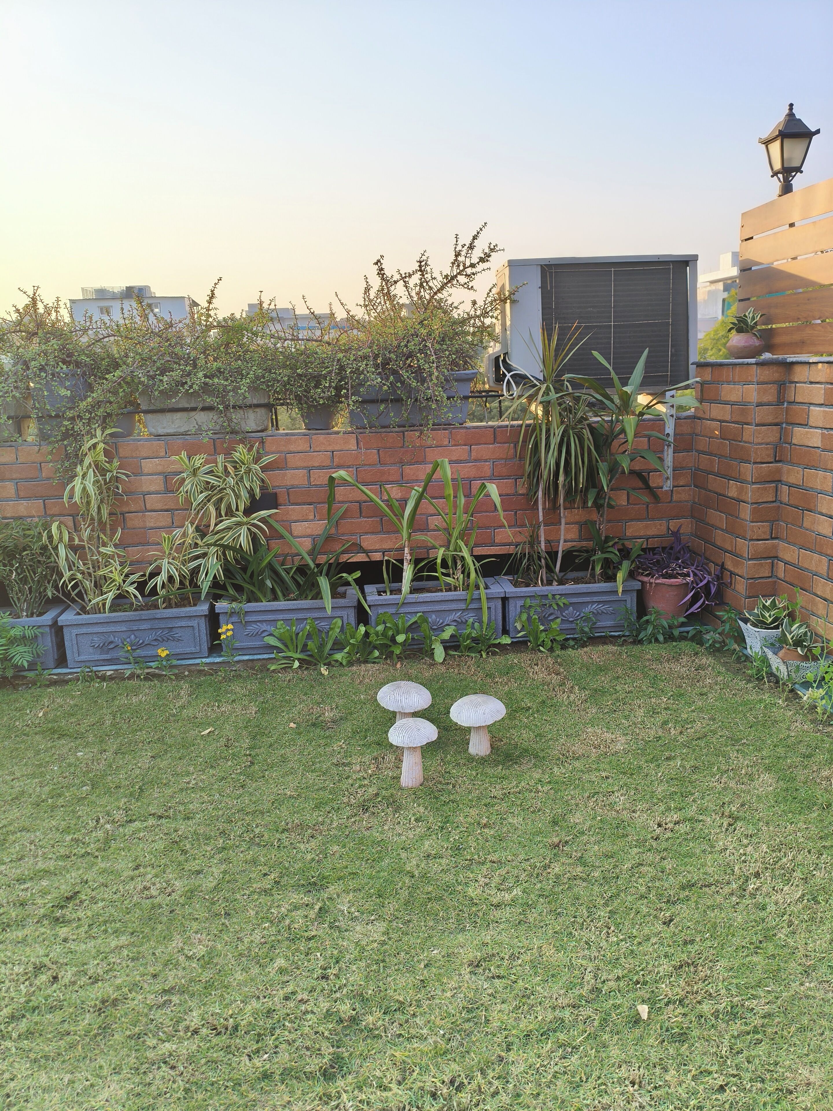 Ein Garten mit Backsteinmauer, Topfpflanzen und einer kleinen Rasenfläche.