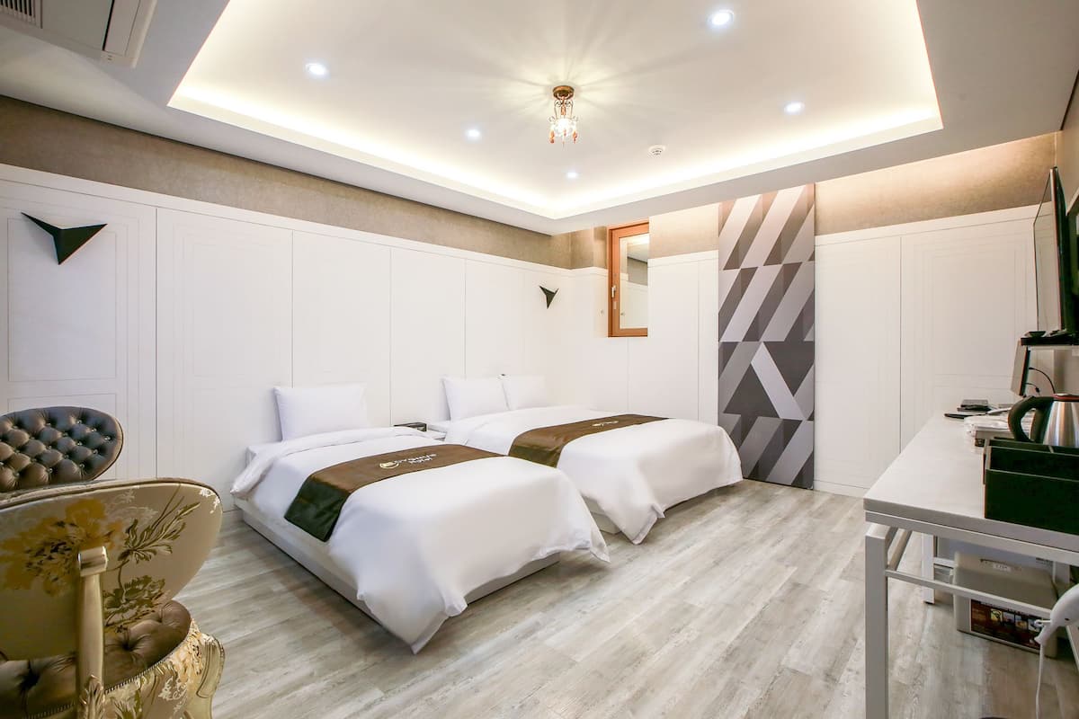 A hotel room with two beds, a desk, and a chair.
