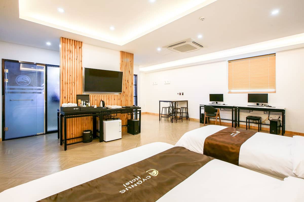 A hotel room with a bed, a desk, a TV, and a window with blinds.