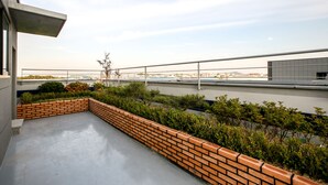 Una terraza en la azotea con una jardinera de ladrillo, vegetación y vistas a la ciudad.
