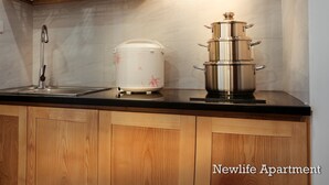Een keuken met houten kastjes, een roestvrijstalen afzuigkap, een spoelbak en een rijstkoker.