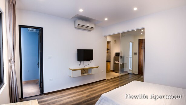 Een moderne slaapkamer met een bed, een wandgemonteerde televisie, een klein schapje en een deur naar een badkamer.