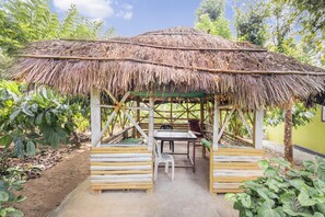 A thatched-roof outdoor seating area with a table and chairs, surrounded by greenery. - GuestHouser 3 BHK Villa e574 (Sulthan Bathery)
