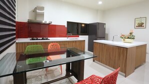 A modern kitchen with a glass dining table, red and green chairs, and a small island with a sink. - Dania Garden (Luodong)