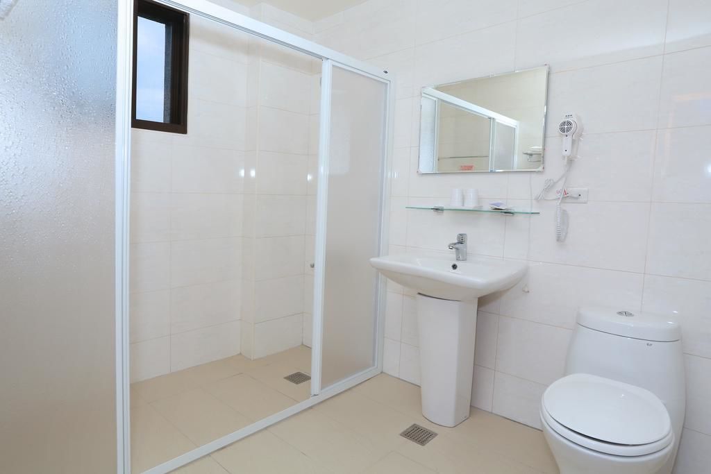 A bathroom with a glass shower enclosure, a pedestal sink, a toilet, and a mirror above the sink.