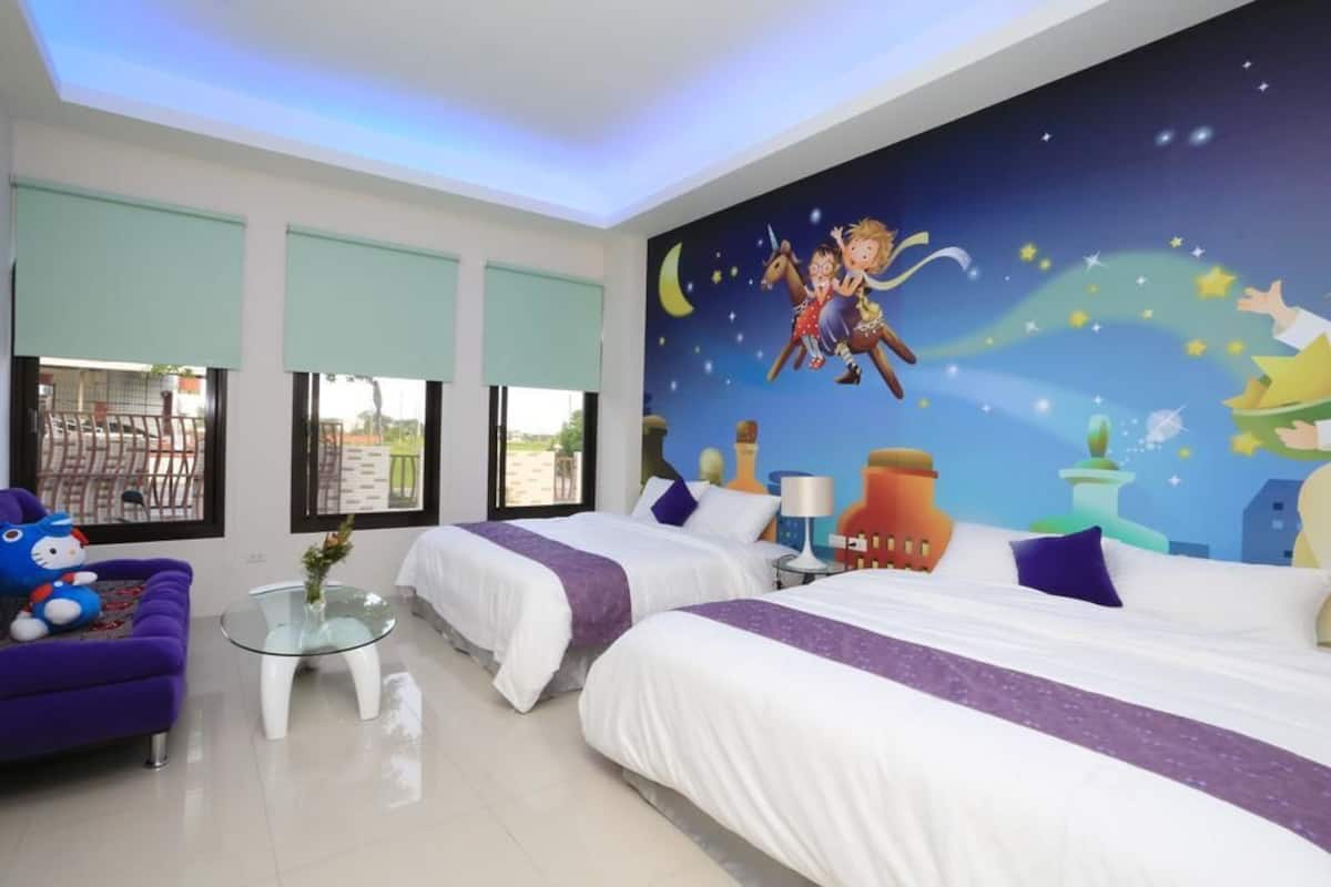 A hotel room with two beds, a purple sofa, a glass coffee table, and a mural of a night scene with stars and a crescent moon.