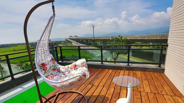 A balcony with a hanging chair, a small table, and a view of a bridge and green fields. - Dania Garden (Luodong)