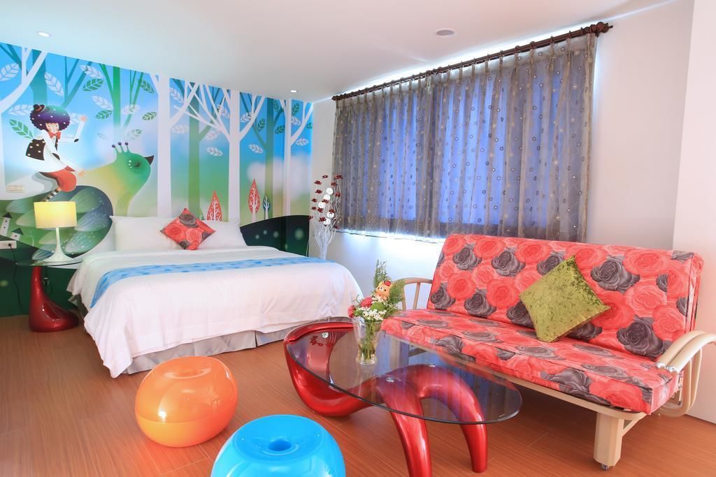 A bedroom with a bed, a sofa, a glass coffee table, and a mural on the wall.