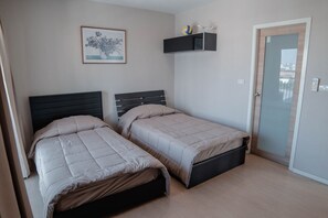 A bedroom with two beds, a framed picture on the wall, a shelf with items, and a door.