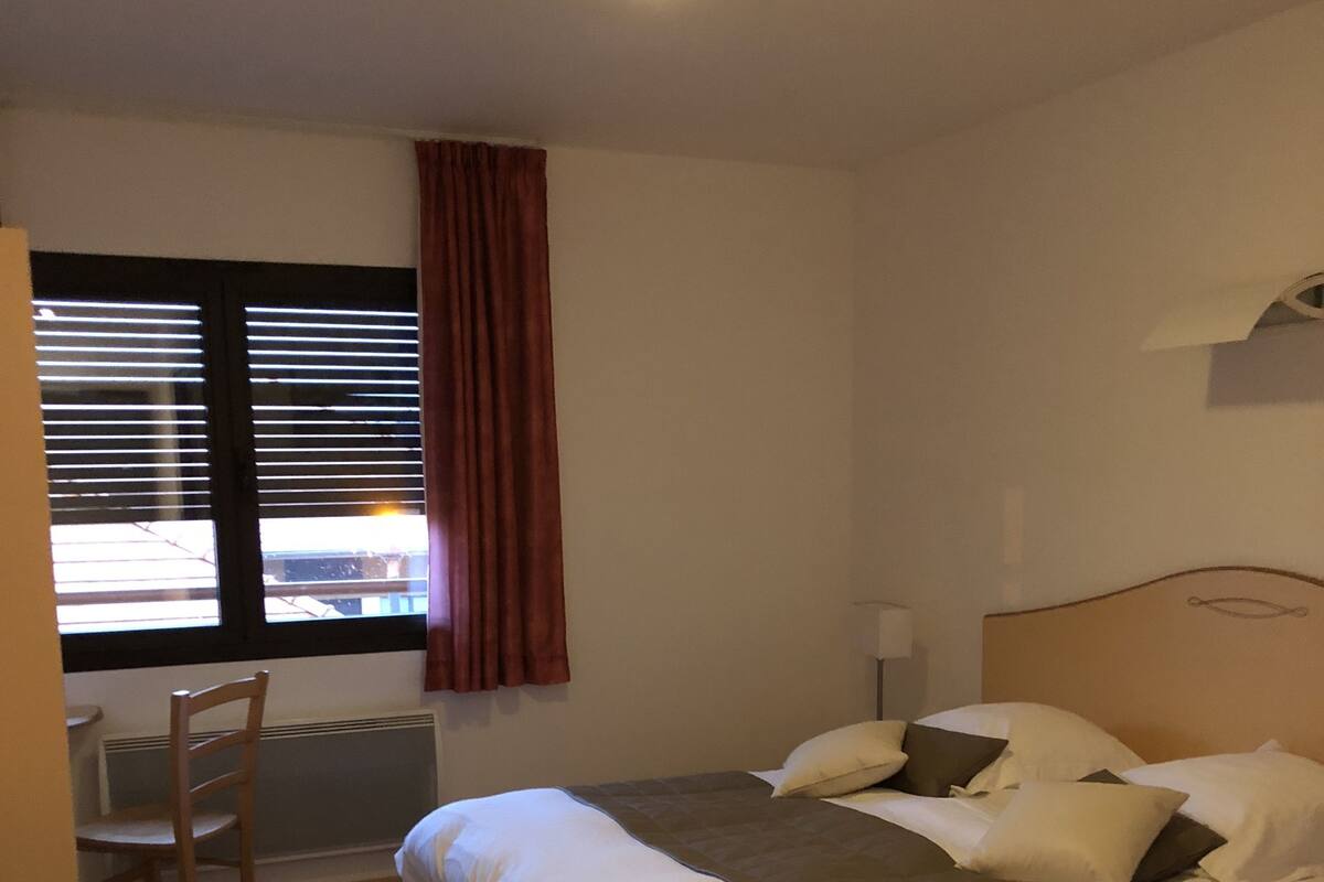 Un dormitorio con cama, una silla, una ventana con persianas y una lámpara de techo.