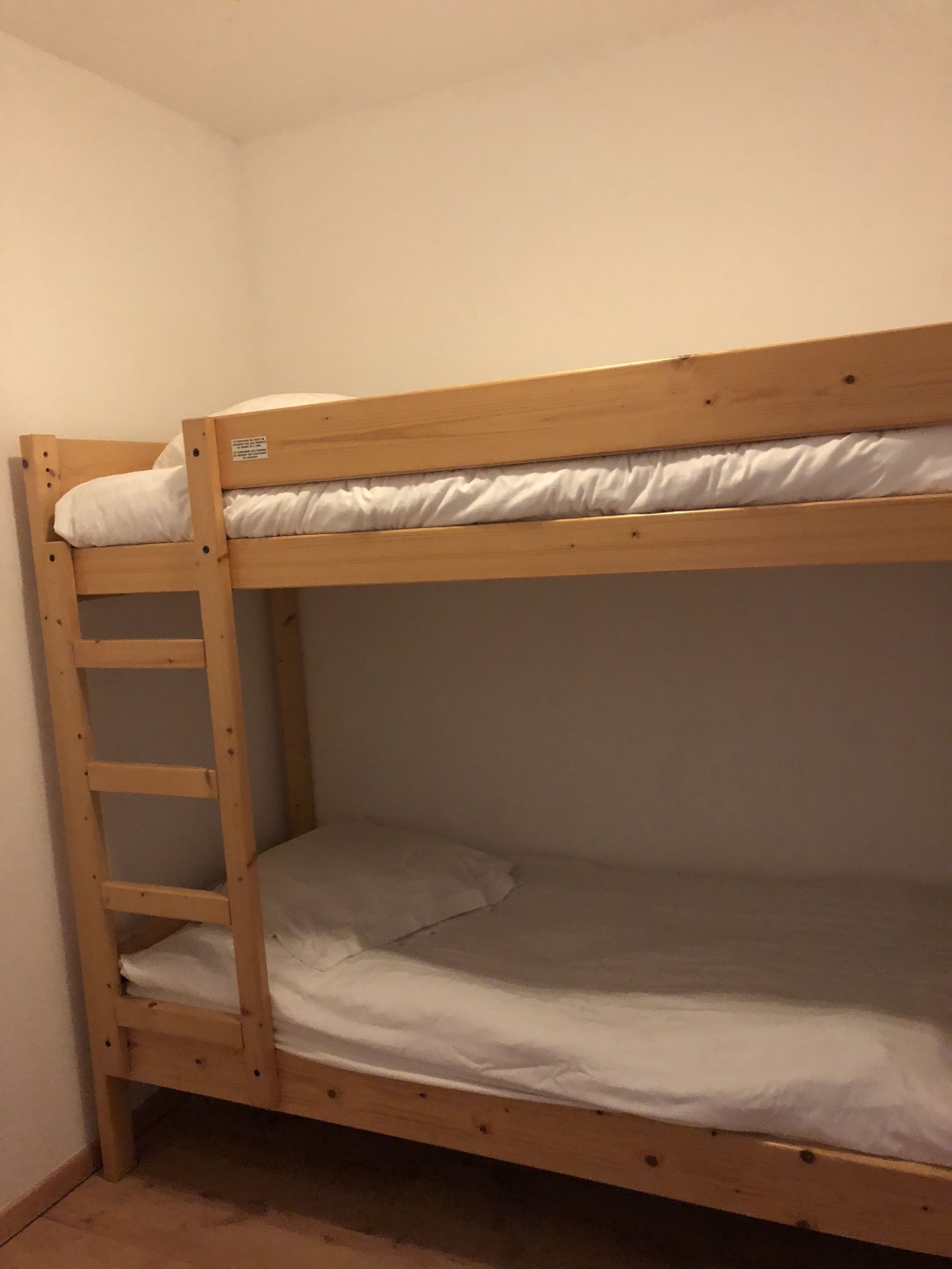 A bunk bed with a wooden ladder, white bedding, and a small shelf.
