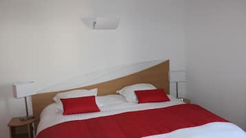 A neatly made bed with red and white bedding, two bedside lamps, and a wall-mounted light fixture.
