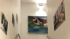 Eine Treppe mit beigefarbenen Stufen und schwarzen Wangen, gesäumt von Metallgeländern, die zu einem Zwischenpodest führt, auf dem ein Haus an einem Fluss gemalt ist.