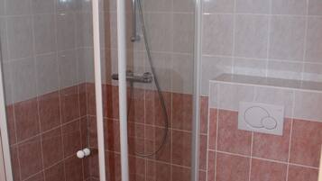 Een badkamer met een douchecabine van glas, een toilet en een betegelde vloer.