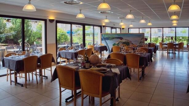 Ein Restaurant mit mehreren Tischen und Stühlen, großen Fenstern und hängenden Pendelleuchten.