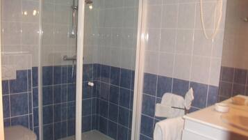 Un baño con ducha envuelta en cristal, un inodoro y un lavamanos con una toalla colgada en la pared.