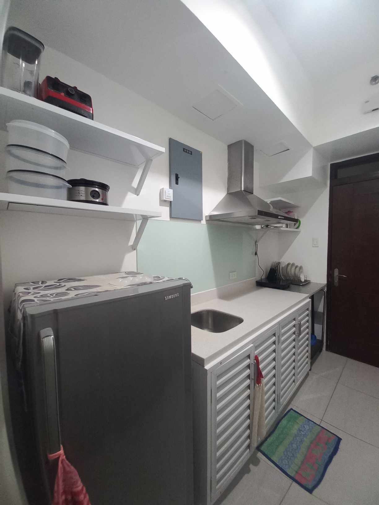 Una cocina con un refrigerador de acero inoxidable, un microondas y una estufa. Hay un lavamanos y un armario con vajilla.