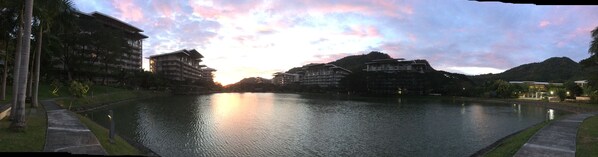 A serene lakeside view with modern buildings, a clear sky, and a calm water surface.
