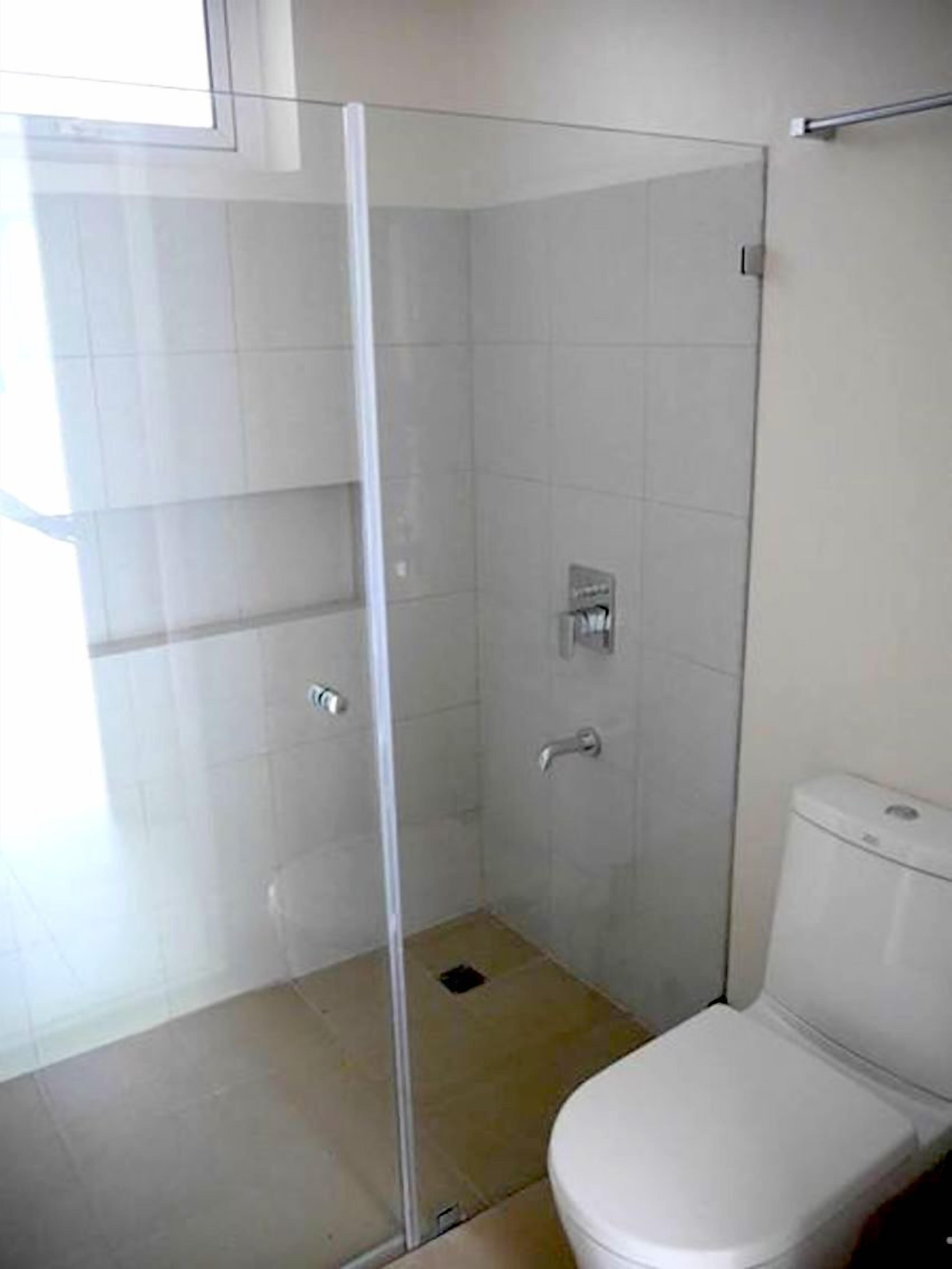 A bathroom with a glass-enclosed shower, a toilet, and tiled walls.