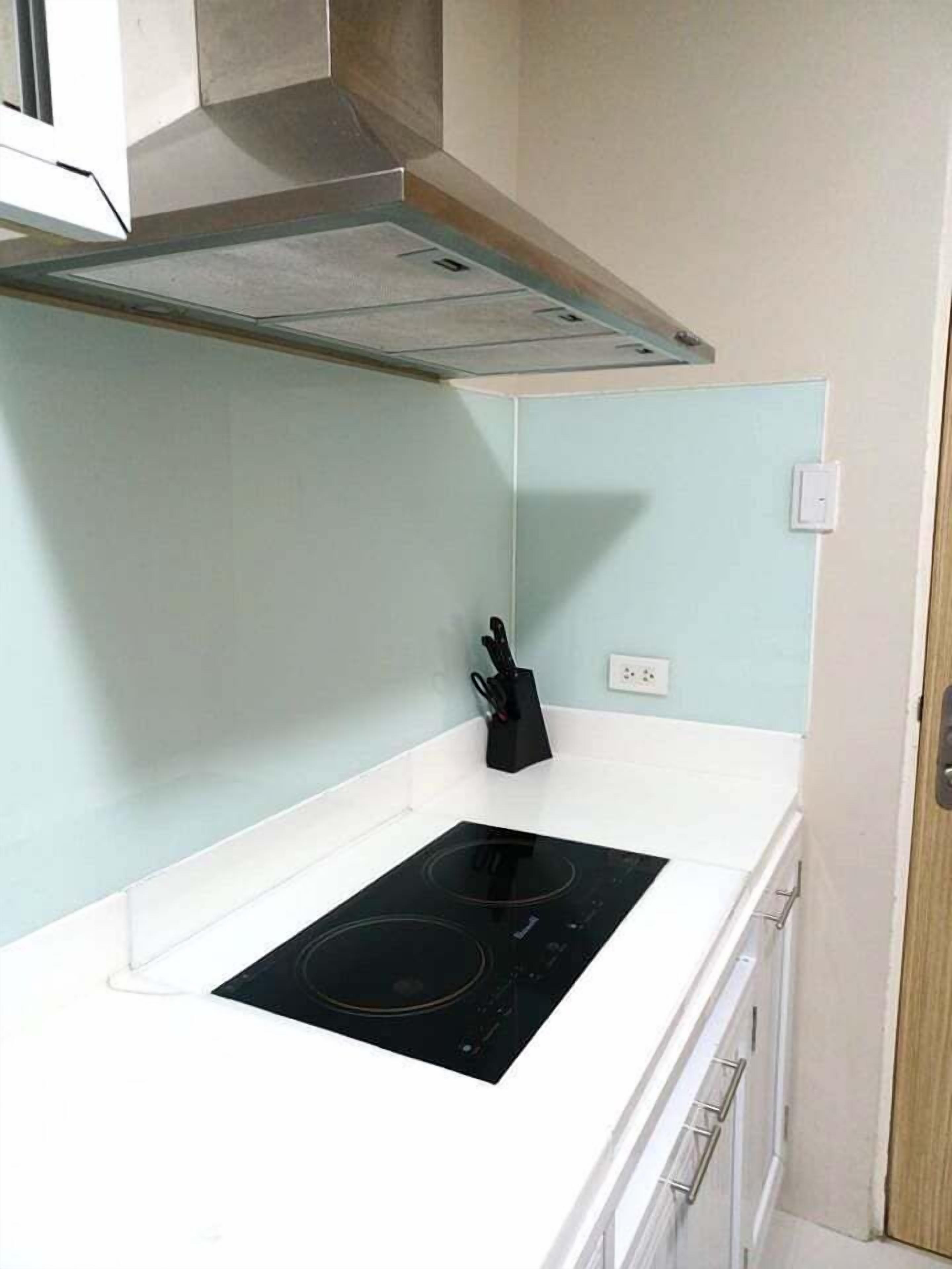 A kitchen with a white countertop, a black induction cooktop, a black knife block, and a stainless steel range hood.