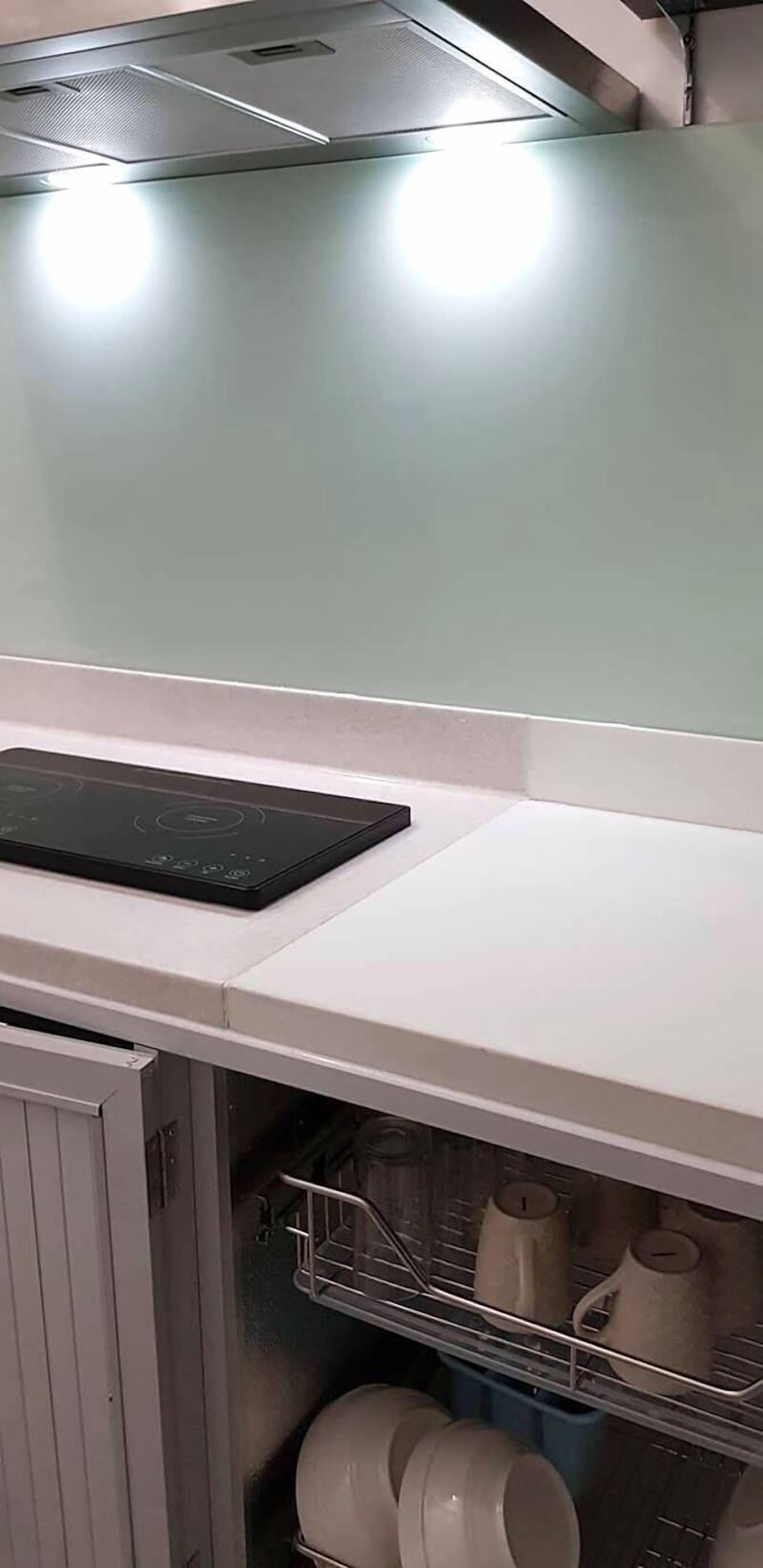 A kitchen with a white countertop, a black induction cooktop, and a dish rack with white dishes.