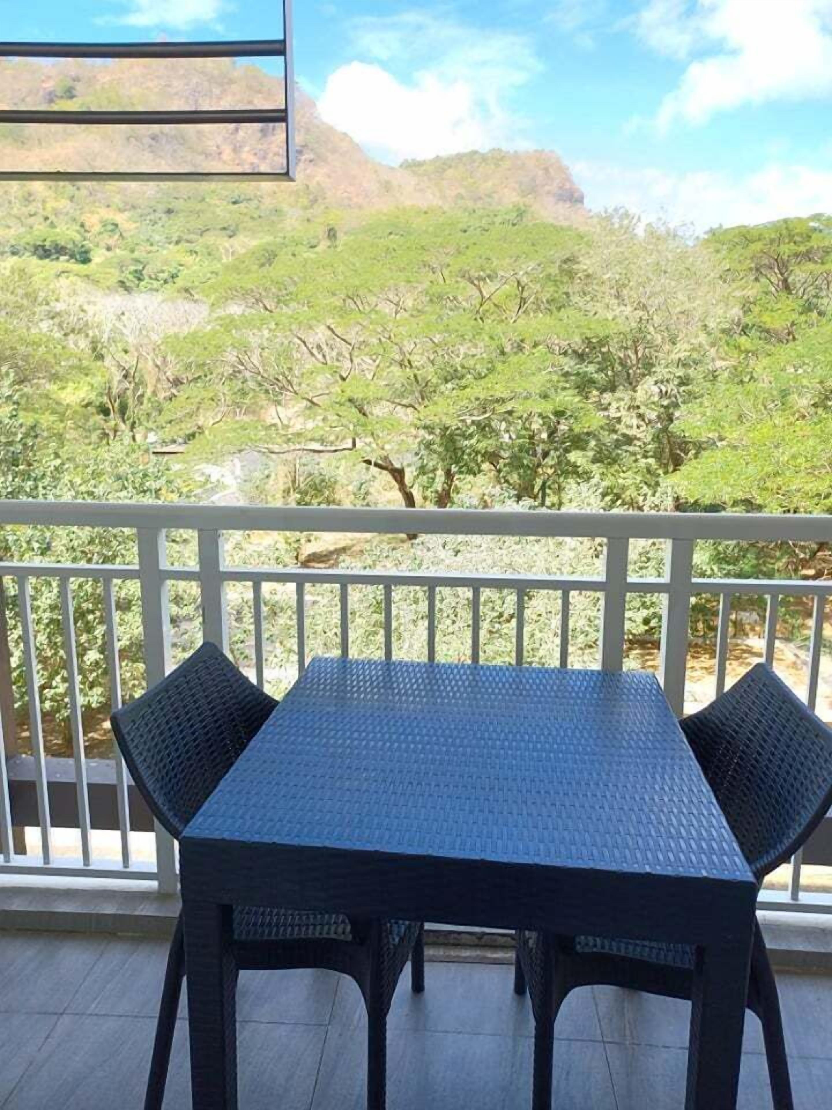 A balcony with a table and chairs, overlooking a lush green landscape with trees and hills.