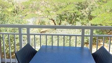 A balcony with a table and chairs, overlooking a lush green landscape with trees and hills.