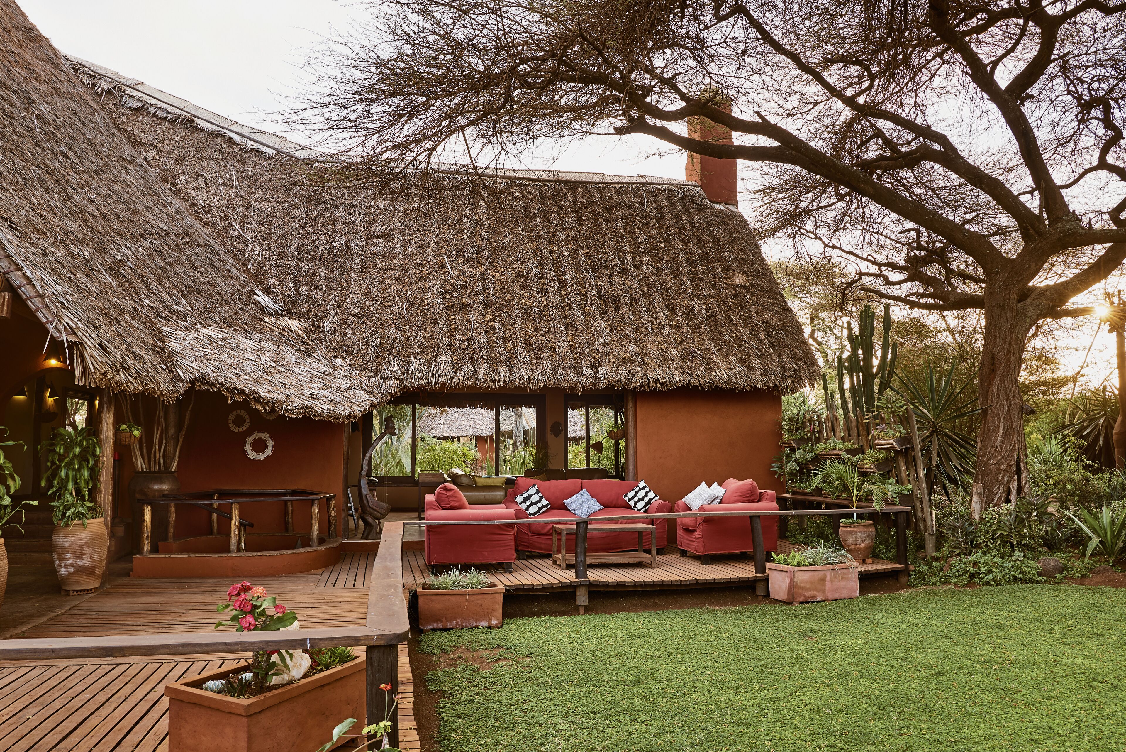 A thatched-roof structure with a wooden deck, red sofas, and potted plants.
